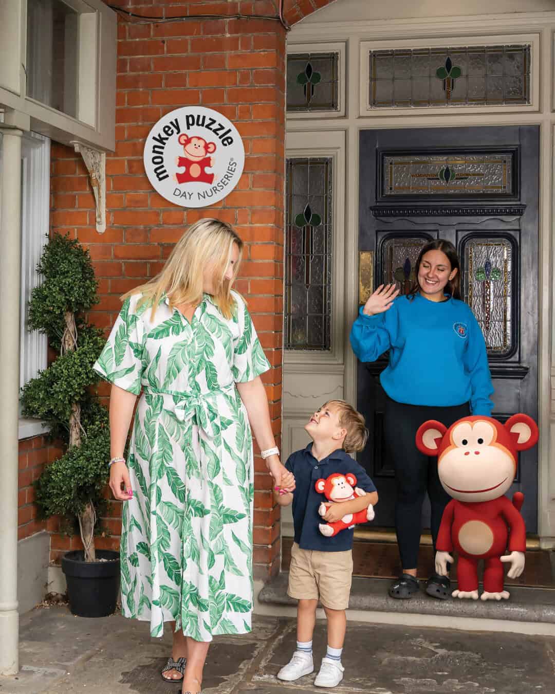 Cute children and staff waving at the door of Monkey Puzzle Day Nurseries, showcasing a welcoming environment for early childhood education and development.