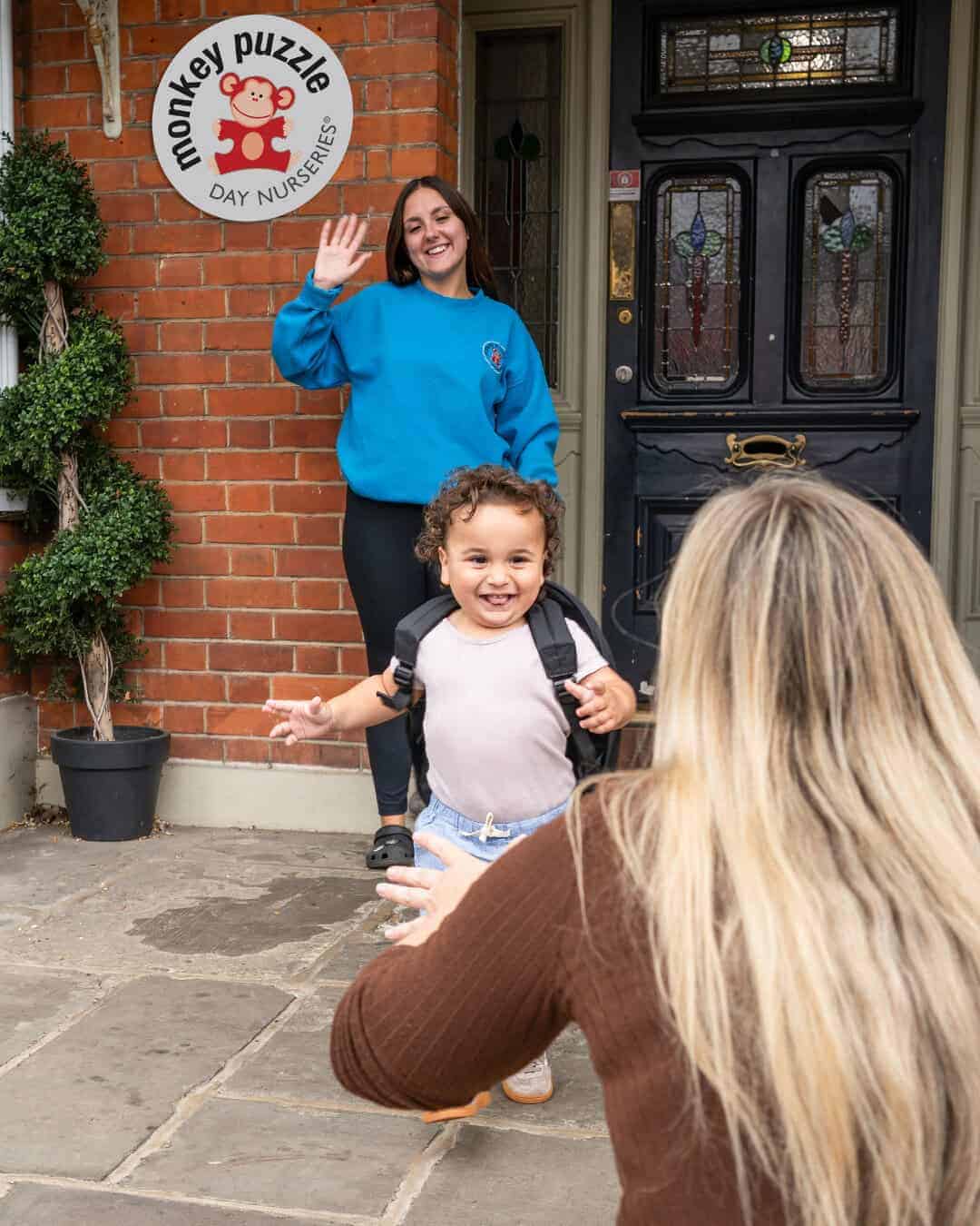 Friendly school staff greeting children at Monkey Puzzle Day Nurseries entrance in a welcoming environment with children and parents.